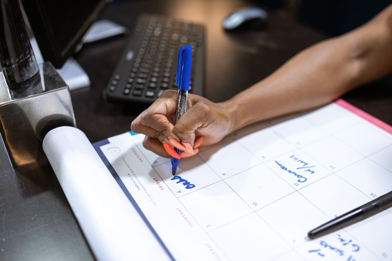 Main notant une date sur un calendrier mural au marqueur bleu pour suivre l'avancée de la grossesse