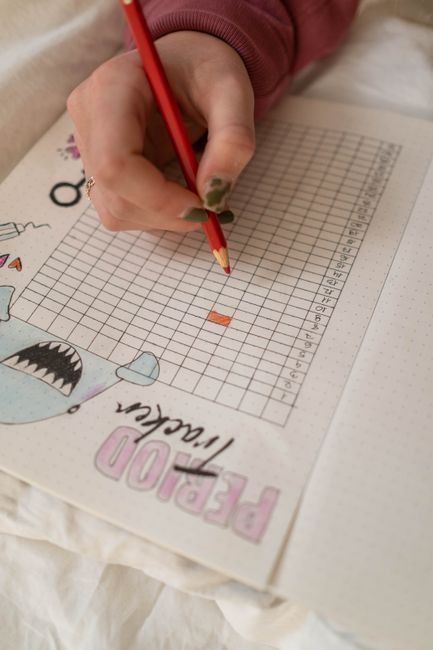 Main notant les dates de son cycle menstruel sur un calendrier papier